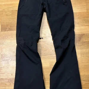 Svarta byxor från Burton - Säljer ett par svarta byxor från Burton i storlek M. De har en cool design med dragkedjor och är perfekta för vintern. Byxorna är gjorda i ett slitstarkt material och har en bekväm passform.