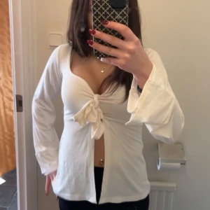 Vit långärmad topp med knyt - Säljer en superfin vit långärmad topp med knyt framtill. Den har en djup v-ringning och är perfekt för både vardag och fest💕