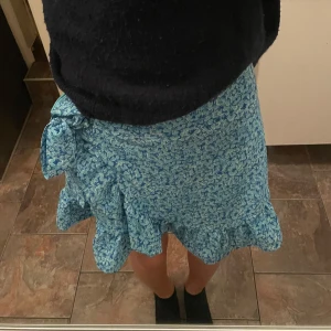 Blå blommig kjol med volang - Superfin blå blommig kjol med volangdetaljer och knytning i sidan.          