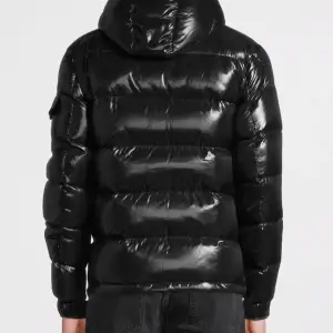 Säljer en snygg svart pufferjacka från Moncler i mycket bra skick. Jackan har en glansig finish och är perfekt för vintern. Den har en dragkedja framtill och långa ärmar. Moncler-loggan är broderad på bröstet. Perfekt för att hålla sig varm och stilren i kylan!