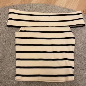 Randig offshoulder topp från Gina Tricot - Säljer en superfin randig offshoulder topp från Gina Tricot i storlek XS. Den är beige med svarta ränder och har en tight passform som sitter snyggt. Perfekt för sommardagar eller en kväll ute. Toppen är i mycket bra skick!