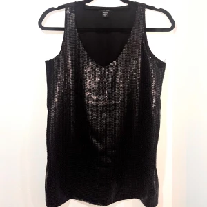 Svart paljettlinne - Snyggt svart linne från täckt med glittrande paljetter. Perfekt för festliga tillfällen! Linnet har en v-ringad design och är ärmlöst. Passar perfekt till en utekväll eller nyårsfesten. ✨