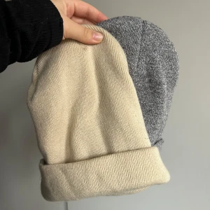 Beige och grå mössa - Två stilrena mössor i beige och grått. Perfekta för kyliga dagar med sin mjuka och bekväma passform. De är ribbade och har en klassisk design som passar till allt. Håll dig varm och snygg i vinter! Båda mössorna för 50 eller 30kr/st