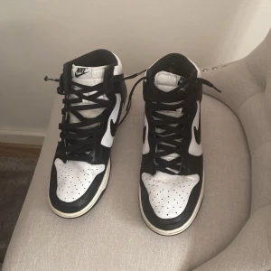  Nike panda sneakers - Säljer ett par klassiska svartvita Nike sneakers i mycket bra skick. De har en snygg hög modell med snörning och den ikoniska Nike-loggan på sidan. Perfekta för både vardag och fest! 🖤🤍 