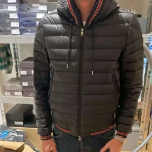 Svart dunjacka från Moncler - Säljer en snygg svart dunjacka från Moncler i mycket bra skick. Jackan har en quiltad design med dragkedja och luva. Den har också Monclers ikoniska logga på ärmen. Perfekt för höst och vinter, håller dig varm och stilren! 🖤