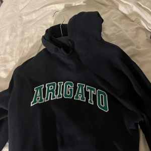 Mörkblå hoodie med texten 'Arigato' - Säljer en snygg mörkblå hoodie med texten 'Arigato' i vitt och grönt på bröstet. Perfekt för en avslappnad stil och passar bra till både jeans och joggers. Den har en klassisk passform och är superbekväm. Perfekt för höst och vår!