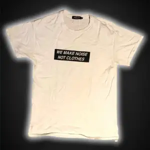 Säljer en vit t-shirt från Undercover med texten 'WE MAKE NOISE NOT CLOTHES' tryckt i svart på framsidan. Den är kortärmad. Perfekt för en avslappnad stil eller som statement-plagg. Skön och stilren design!