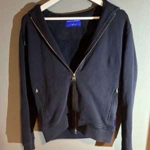 Marin blå hoodie med dragkedja från tiger of sweden - Säljer en Marin blå hoodie från Face of Sweden i bra skick. Den har en dragkedja framtill och långa ärmar. Perfekt för höst och vinter, och passar till både vardag och chill. Hör av dig om du är intresserad!