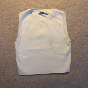 Vit ärmlös topp från Zara - Säljer en stilren vit ärmlös topp från Zara i storlek M. Perfekt som ett basplagg i garderoben. 