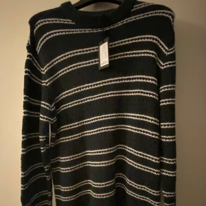 Grön svart och vit randig tröja - Säljer en snygg grön tröja med vita svarta ränder. Den är perfekt för kyliga dagar och har en klassisk design med långa ärmar. Tröjan är i bra skick och passar både till vardags och lite finare tillfällen. Taggen sitter kvar.