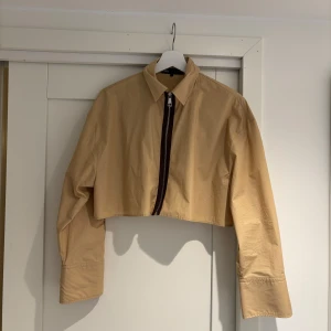 Croppad skjorta - Beige skjorta i croppad modell med brun detalj runt dragkedjan!🫶🏻