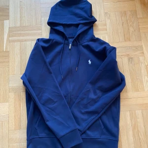 Mörkblå hoodie  - Säljer en snygg mörkblå hoodie från Ralph Lauren med dragkedja och den klassiska loggan på bröstet. Perfekt för kyliga dagar och har en skön passform. Den är i mycket bra skick och redo för nya äventyr!