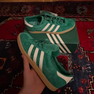 Adidas Gazelle Södermalm  - Helt nya! Sneakersnstuff hyllar den plats som gav oss ett hem: Södermalm. Ön på södra sida om Sveriges huvudstad har varit SNS hjärta sedan 1999. Självklart måste den få sin egen sneaker. Och det har den fått, en  modell i grönt och vitt, Södermalms färger. Den klassiska skon från the adidas City Series är gjord i mjuk mocka med vita läderränder, ”Södermalm” i guld metallic och en gummiyttersula. 