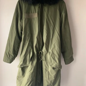 Olivgrön parkajacka med svart päls foder - Jag säljer min MR and Mrs Smith parka - Superpris! Militärgrön parka med svart pälsfoder, som man kan ta av för anpassning till olika väder. Jackan har en elegant lammskinns trim och är otroligt varm & stilren. Perfekt för vinter och kyliga dagar. Jack är utan defekter i fint skick. Helt äkta utan några fusk detaljer. Passa på att få en kvalitets jacka till ett fantastiskt pris!