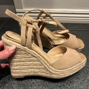 Beige kilklackssandaler - Snygga beige sandaler med kilklack i repmaterial. De har en öppen tå och justerbara remmar för perfekt passform. Perfekta för sommarens alla tillfällen, både till vardags och fest. Superbekväma och stilrena!