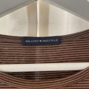 Brunrandig topp från Brandy Melville - Säljer en superfin brunrandig topp från Brandy Melville. Den är kortärmad och har en normal passform, perfekt för både vardag och fest. Materialet är mjukt och bekvämt, vilket gör den idealisk för alla säsonger. Passar perfekt till jeans eller kjol!