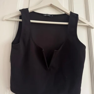 Svart ärmlös topp från Nelly - Snygg svart ärmlös topp från Nelly i ett stilrent och enkelt snitt. Perfekt för både vardag och fest. Toppen har en djup v-ringning och är gjord i ett mjukt och bekvämt material. 