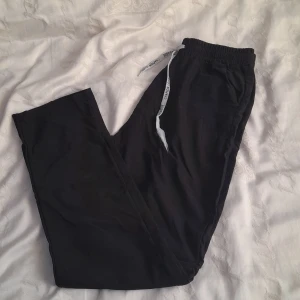 Svarta linnebyxor som är perfekta för sommaren eller att bara ha hemma som mjukisbyxor  - Säljer ett par svarta linnebyxor/mjukisbyxor i bra skick. De har en elastisk midja med snörning där det står 'CHAPION LEAGUE. Byxorna är bekväma och har en loose passform.