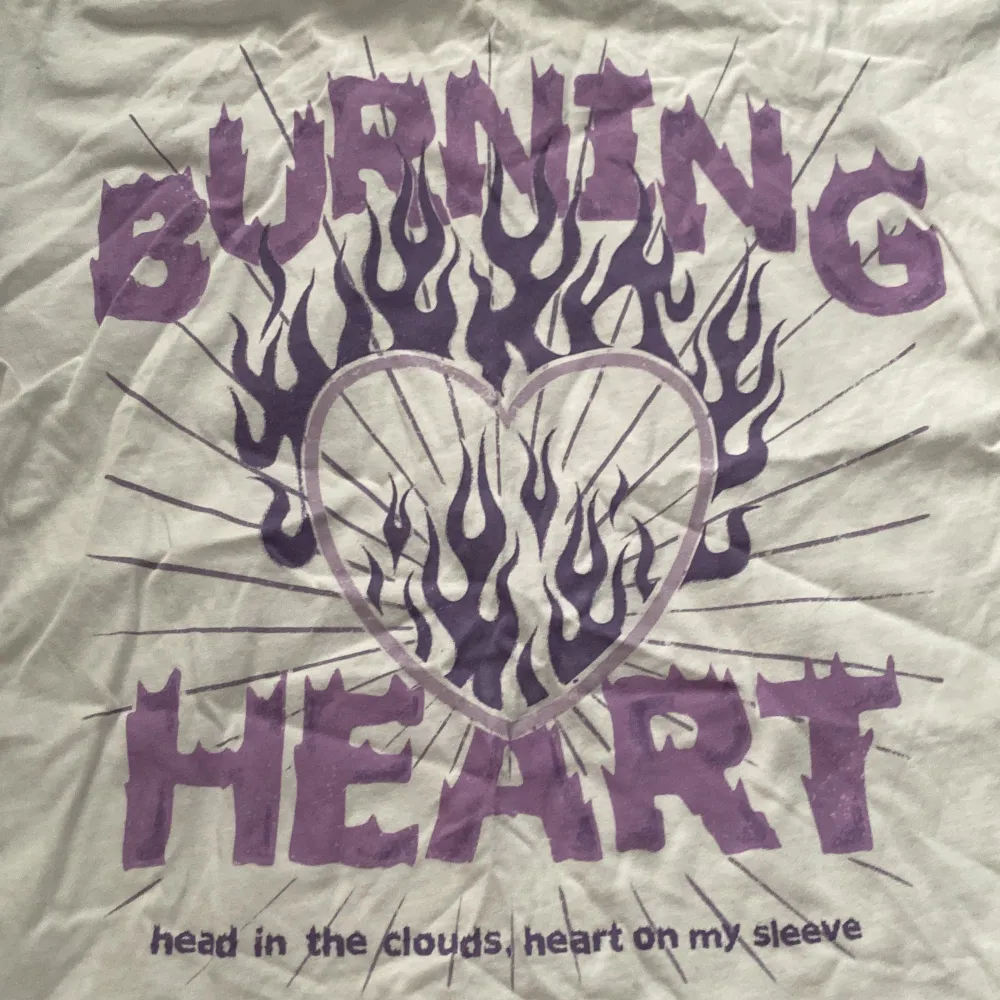 Cool vit t-shirt från Lindex Kids med ett stort lila tryck som säger 'Burning Heart' och ett hjärta med flammor.  T-shirten är i bomull och har korta ärmar. Passar bra till både vardag och lek.. T-shirts.