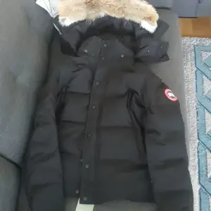 Säljer en svart dunjacka från Canada Goose i mycket bra skick. Jackan har en avtagbar huva med pälsdetaljer och stängs med dragkedja och knappar. Perfekt för kalla vinterdagar! 🖤