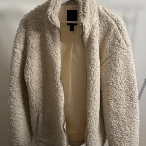 Beige teddyjacka från New Look - Mysig beige teddyjacka från New Look i storlek herr XS. Perfekt för kyliga dagar med sitt fluffiga material och dragkedja framtill. Jackan har en enkel och stilren design som passar till det mesta. Ett måste för höst- och vintergarderoben!