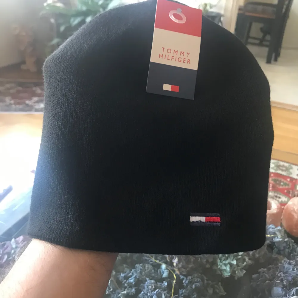 Snygg och stilren svart mössa från Tommy Hilfiger i nytt skick. Den är perfekt för kalla dagar och har en liten broderad logga i rött, vitt och blått framtill. Passar både till vardags och mer uppklädda tillfällen. Ett måste för vintern!. Accessoarer.