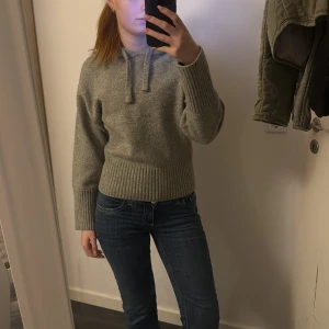 Grå stickad hoodie - Mysig grå stickad hoodie med långa ärmar och ribbade muddar. Perfekt för kyliga dagar och ger en avslappnad stil. Den har en bekväm passform och en klassisk huva med dragsko.