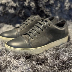 Lanvin Captoe - Säljer ett par stilrena sneakers från Lanvin. De har en klassisk design med snörning och en kontrasterande vit sula. Perfekta för både vardag och festliga tillfällen. Skorna är skick 8/10 och kommer i originalkartong. Finns en liten skråma på captoen skicka pm för bild!⚜️
