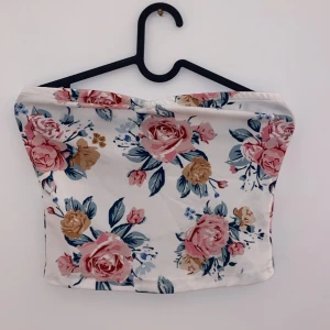Blommig tubtopp - Säljer en superfin blommig tubtopp i vitt med stora rosa och beige rosor samt gröna blad. Perfekt för sommardagar eller en festlig kväll. Toppen är i ett mjukt och bekvämt material som sitter skönt mot huden.