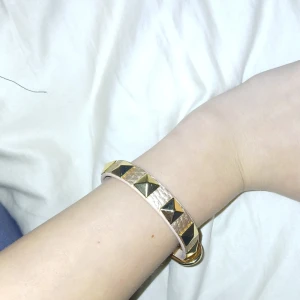 Guldarmband med nitar - Snyggt guldarmband med coola pyramidformade nitar. Armbandet har en justerbar rem med ett spänne för perfekt passform. Perfekt för att ge din outfit en edgy touch!