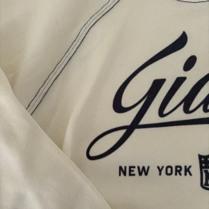 Vit sweatshirt med Giants-tryck - Säljer en snygg vit sweatshirt med Giants-tryck i indigoblå ’sammetstryck’ och matchande dekorativa sömmar. Tröjan har  ribbade muddar vid ärmslut och nederkant. 