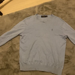 Ljusblå tröja från Polo Ralph Lauren - Säljer en stilren ljusblå tröja från Polo Ralph Lauren i bra skick. Den är perfekt för både vår och höst med sin mjuka bomullskänsla. Tröjan kostar runt 1500 ny pris, men på grund av några användningar så sänker jag priset.