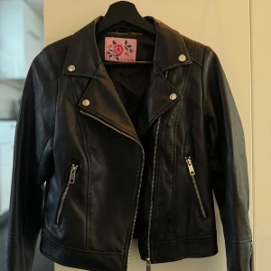 Svart skinnjacka med dragkedja - Säljer en snygg svart skinnjacka i mycket bra skick. dragkedja och silverfärgade knappar. Perfekt för höst och vår, och funkar lika bra till fest som till vardags. Jackan har långa ärmar och två praktiska fickor med dragkedja framtill. Frakt ingår.