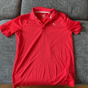 Röd pikétröja från Puma - Säljer en snygg röd pikétröja från Puma, perfekt för golf eller vardagsbruk. Tröjan har korta ärmar och en klassisk krage med knappar. Materialet är lätt och andas bra, vilket gör den idealisk för varmare dagar. Passar både till sport och casual outfits. 🏌️‍♂️Pris går alltid att förhandlads!