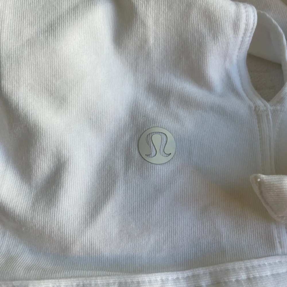 Säljer en superfin vit linnetopp från Lululemon. Den är ärmlös och har en snygg knytning i ryggen som ger en cool look. Perfekt för träning eller en varm sommardag. Materialet är mjukt och bekvämt, vilket gör den idealisk för både aktivitet och avslappning.. Toppar.