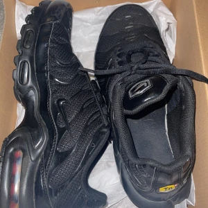 Nike Tns  - Säljer ett par svarta Nike sneakers i mycket bra skick. De har en cool design med synlig dämpning i sulan och klassisk snörning. Perfekta för både vardag och träning. Skorna är i storlek herr 42,5 och kommer i originalkartong.ÄKTA!!!PRISET KAN DISKUTERAS 