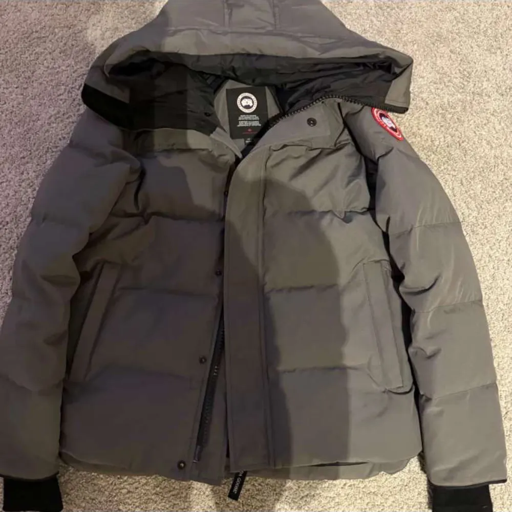 Säljer en grå dunjacka av Canada Goose i mycket bra skick. Jackan har en praktisk huva och dragkedja framtill. Perfekt för kalla vinterdagar. Den är i storlek M och har en snygg, stilren design.. Jackor.