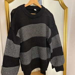 Randig glittrig stickad tröja - Säljer en supermysig stickad tröja från HM med breda svarta och grå ränder. Perfekt för kyliga dagar med sin avslappnade passform och långa ärmar. Den har en klassisk rund halsringning och är i mycket bra skick. Passar perfekt till både jeans och kjol!