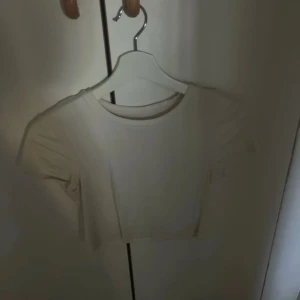 Vit croppad topp från new yorker strl M - Säljer en snygg vit croppad topp från New yorker i storlek M. Perfekt för sommardagar eller som ett lager under en jacka. Toppen är i bra skick och har en enkel, stilren design. Passar till både jeans och kjol!