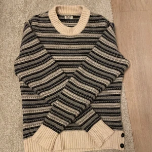 Randig stickad tröja från Acne - Säljer en superfin randig stickad tröja från Acne Jeans i storlek M. Den har en mysig beige bas med svarta och grå ränder. Perfekt för höst och vinter med sina långa ärmar och ribbade detaljer vid hals och ärmslut. Knappar på sidan ger en extra touch. Passar både till vardags och lite finare tillfällen! Skriv vid minsta lilla fundering😀✍️✅