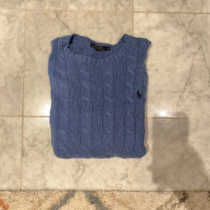 Blå stickad tröja från Polo Ralph Lauren - Säljer en snygg blå stickad tröja från Polo Ralph Lauren. Den har ett klassiskt flätmönster och en liten broderad logga på bröstet. Perfekt för kyliga dagar och passar både till vardags och lite finare tillfällen. Tröjan är i mycket bra skick och supermjuk!