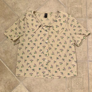 Kortärmad blommig skjorta  - Ljusgul kortärmad skjorta med lila blommor i storlek S, lätt Croppad. Skjortan är i gott begagnat skick och är enbart använd fåtal gånger. Klicka gärna på köp nu och meddela för eventuella frågor. :)
