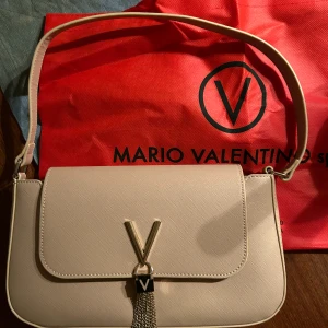 Beige axelväska från Valentino - Säljer en elegant beige axelväska från Mario Valentino i mycket bra skick, använd 2 gånger av min mamma men hon ville inte ha kvar dom så bad mig sälja dom. Insidan har en dragkedja för extra säkerhet. Kommer med originalpåsen