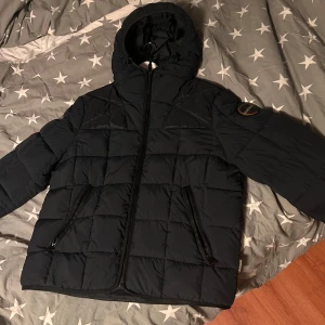 Mörkblå jacka från Napapijri - Säljer en mörkblå pufferjacka från Napapijri i storlek L men passar även M. Jackan är quiltad och har en dragkedja framtill. Den är perfekt för kalla dagar med sin varma och sköna passform. Ordinarie pris runt 2500kr. Jackan är i fint skick. Pris går att diskutera vid snabb affär!