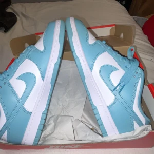 Nike Dunk i ljusblått och vitt - Säljer ett par Nike Dunk i superfräscht ljusblått och vitt. De är i nytt skick och kommer i originalkartong. Perfekta för både vardag och fest! Skorna har en klassisk design med snörning och en bekväm passform. Missa inte chansen att äga dessa snygga sneakers! 💙
