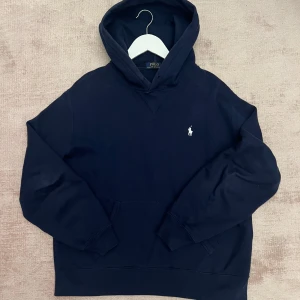 Hoodie Ralph Lauren - Säljer en snygg mörkblå hoodie från Polo Ralph Lauren. Den har en klassisk design med en liten vit logga på bröstet och en bekväm huva. Perfekt för både höst och vinter. 