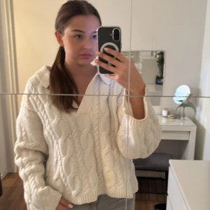 Vit stickad tröja - Mysig vit stickad tröja med kabelstickat mönster. Perfekt för kyliga dagar med sin avslappnade passform och långa ärmar. Den har en v-ringad hals och är superbekväm att bära. Passar perfekt till jeans eller leggings för en casual look.