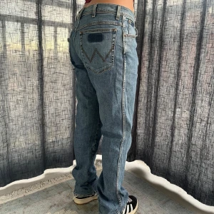 Unika Wrangler jeans  - Säljer ett par blå jeans i bra skick med coola slitna detaljer på bakfickan. Storlek 35/34 Midjemått 42 cm Grenmått 26 cm innerbenslängd 84 cm