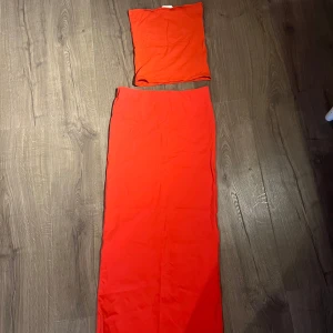 Röd tvådelad klänning - Säljer en snygg röd tvådelad klänning i nytt skick. Setet består av en axelbandslös topp och en långkjol, perfekt för sommarens fester. Materialet känns mjukt och stretchigt, vilket ger en bekväm passform. Toppen och kjolen kan bäras tillsammans eller matchas med andra plagg för olika stilar. Perfekt för en dag på stranden eller en kväll ute! 🌟
