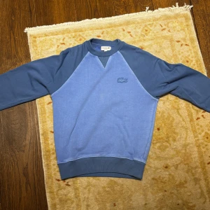Blå sweatshirt från Lacoste - Säljer en blå sweatshirt från Lacoste i relaxed fit. Riktigt snygg tvätt på tröjan, väldigt svår att få tag i.